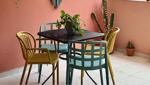 Un balcón con mesa y sillas, cestas colgantes con plantas y adornos de macramé en la pared.