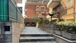 A narrow pathway leading to a building with multiple balconies and a green fence on one side.