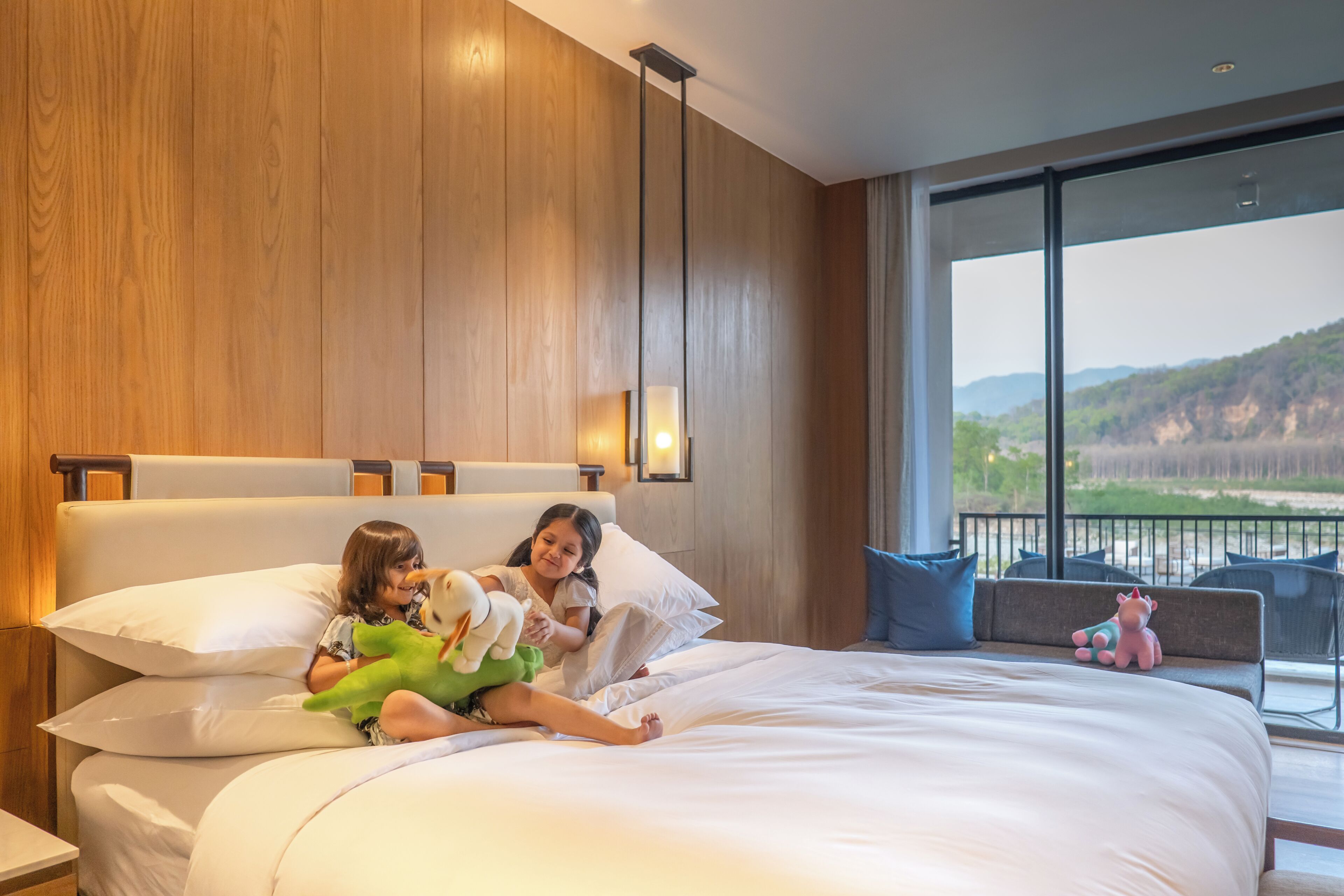 A bedroom with a large bed, a nightstand, a window with a view of the outdoors, and a balcony with chairs.