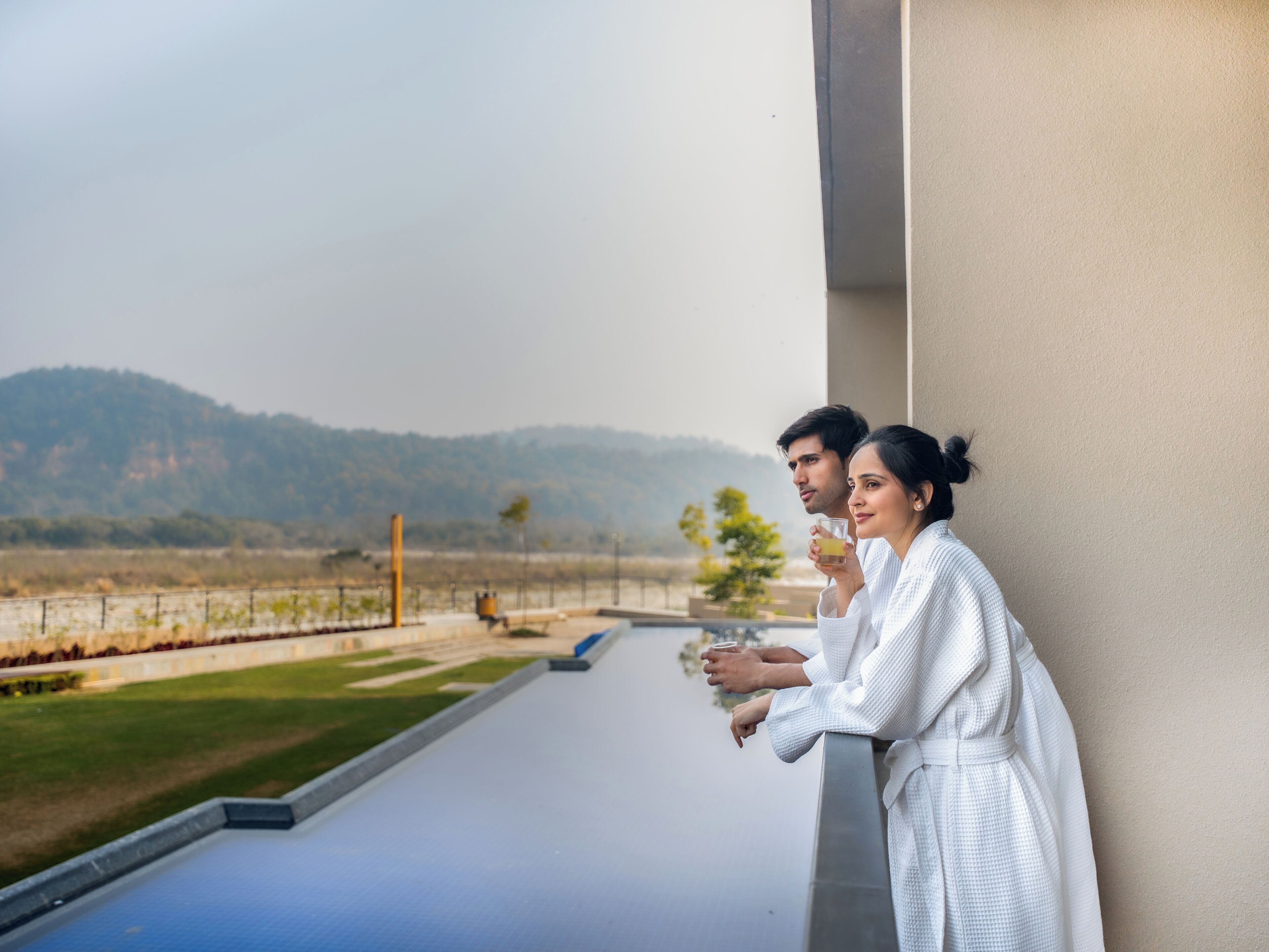 Una pareja en un balcón con vistas a un jardín y colinas.