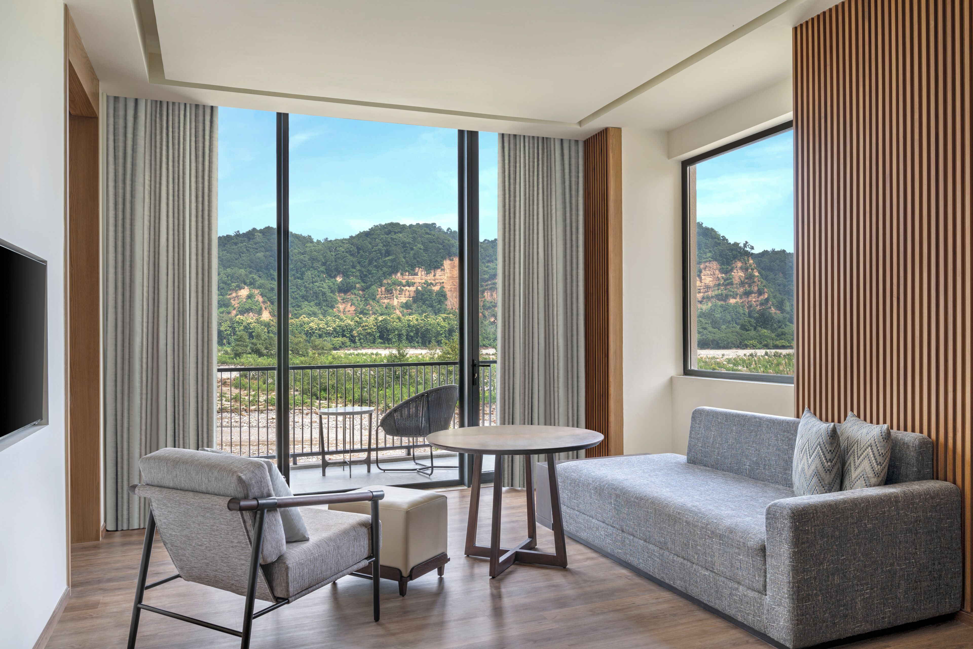 A modern hotel room with a balcony, a sofa, a chair, and a small table.