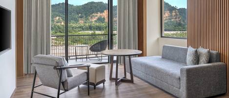A modern hotel room with a balcony, a sofa, a chair, and a small table.