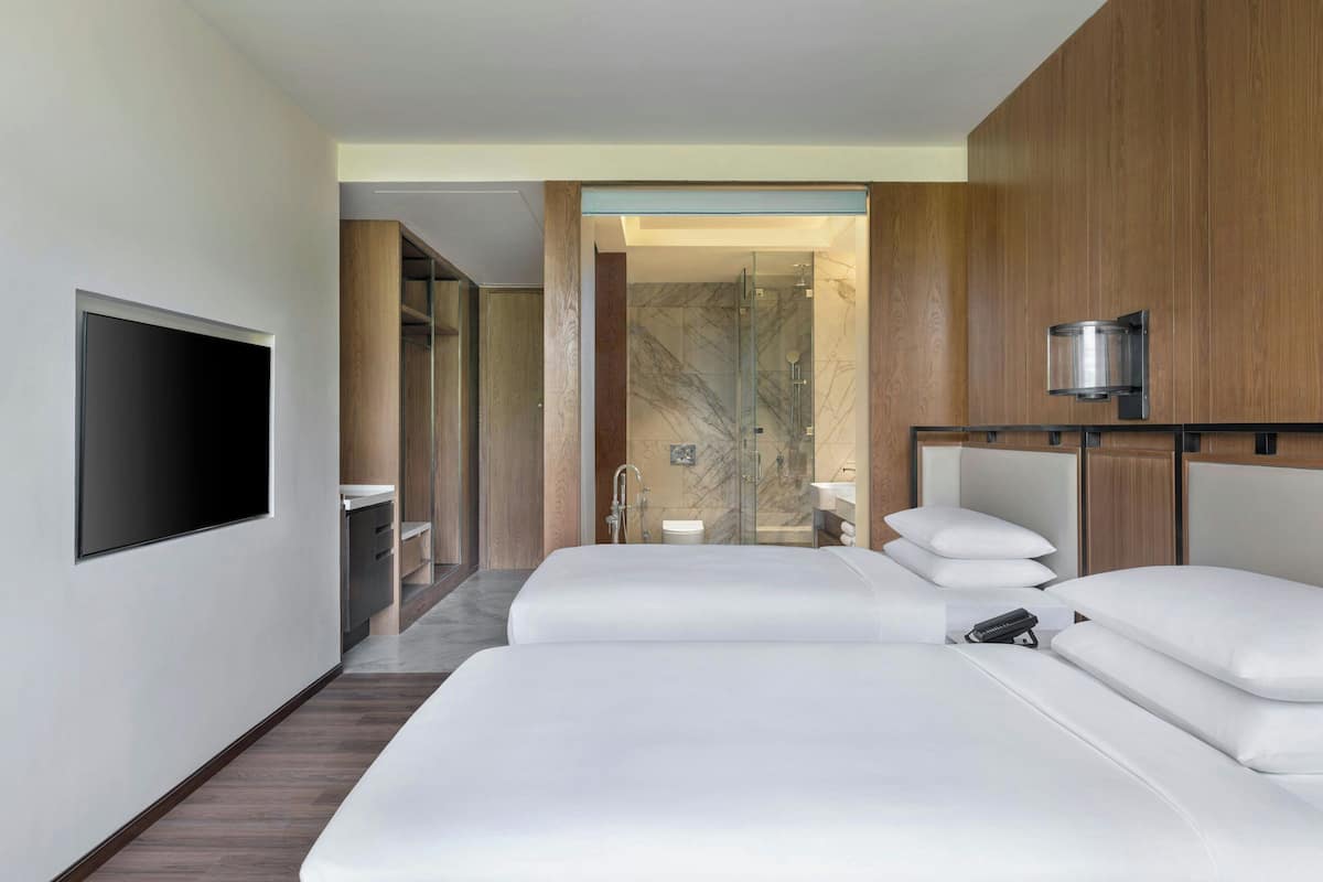 A modern hotel room with two beds, a TV, a shower, and a bathroom with a marble wall.