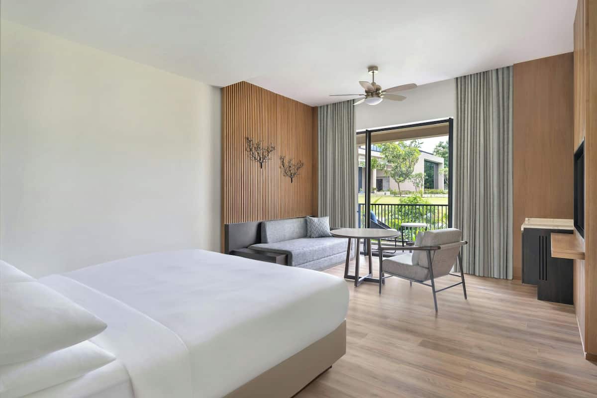 A hotel room with a bed, a sofa, a small table, and a balcony with a view of the outside.