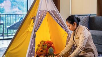 A person playing chess inside a yellow tent with star patterns, located in a room with a view of greenery.