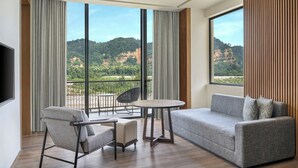 Een moderne hotelkamer met balkon, een bank, een stoel en een klein tafeltje.