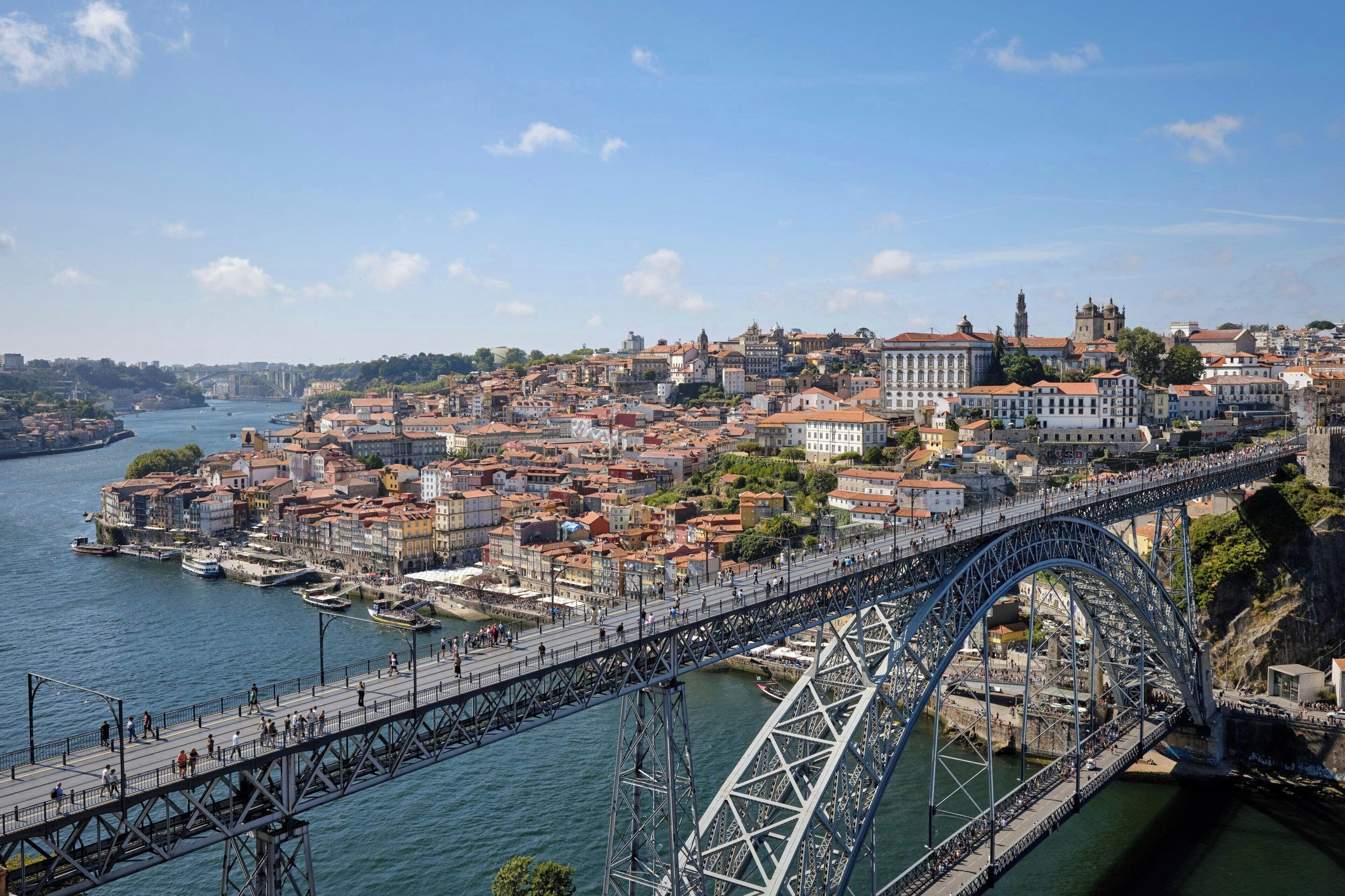 Uma grande ponte de aço que atravessa um rio, ligando duas áreas urbanas densamente povoadas com edifícios históricos.