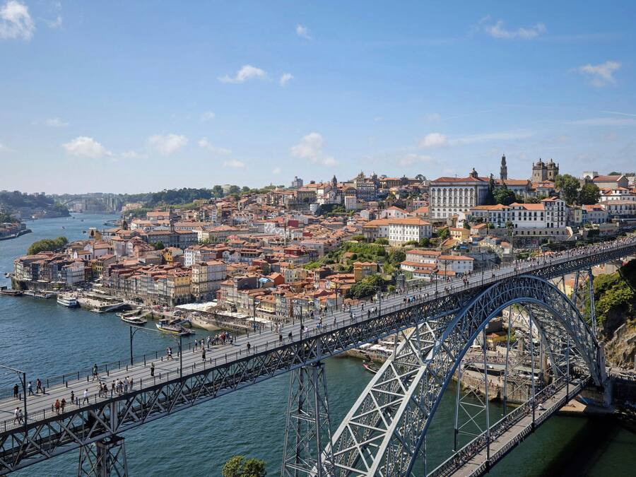 Uma grande ponte de aço que atravessa um rio, ligando duas áreas urbanas densamente povoadas com edifícios históricos.