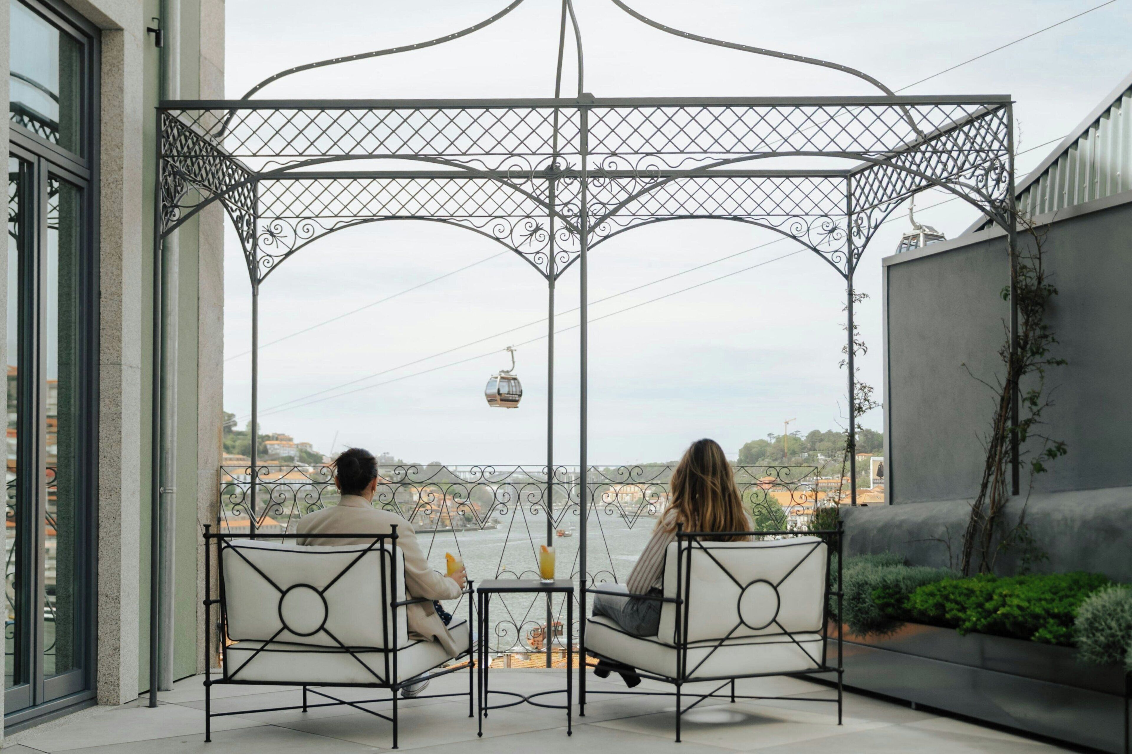 Two people seated at a table under a metal gazebo with a view of a cable car and buildings in the distance.