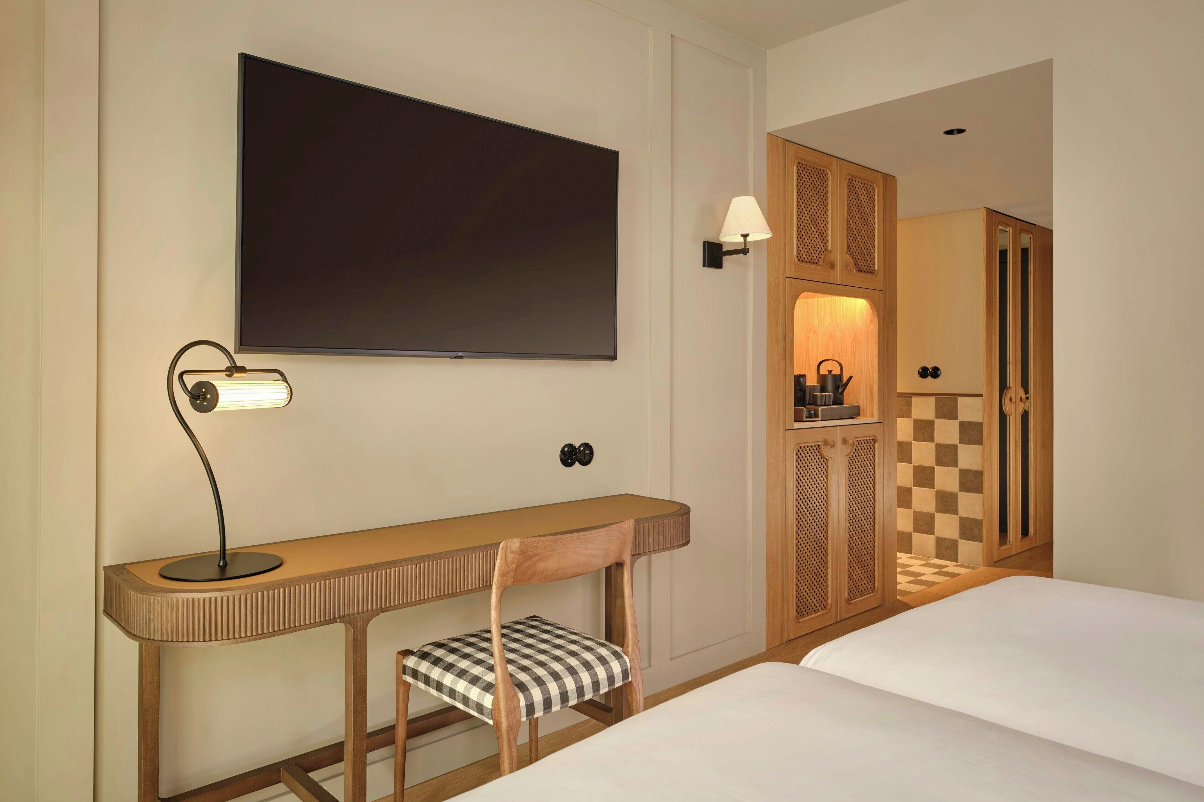 A hotel room with a bed, a desk with a chair, a television, and a wardrobe.