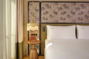 Una habitación de hotel con una cama, una mesita de noche con lámpara y una pared con diseño decorativo.