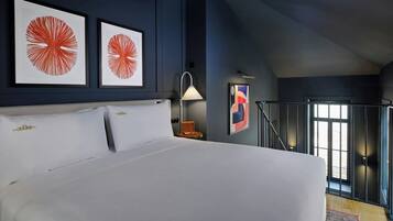 Um quarto com uma cama grande, obras de arte nas paredes, uma mesa de cabeceira com abajur e vista para uma varanda.