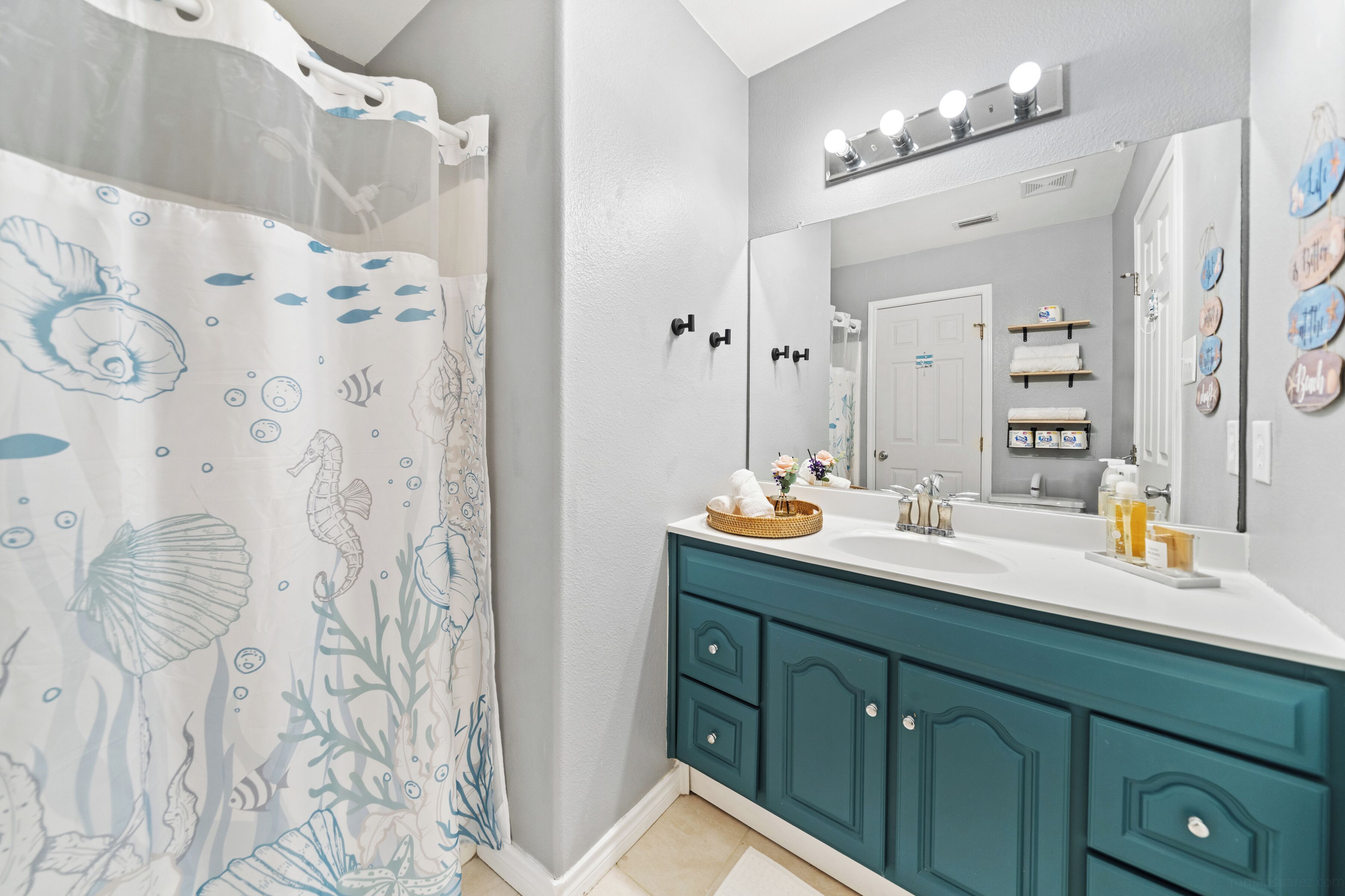 A bathroom with teal cabinets, a white sink, and a shower curtain with sea life designs.