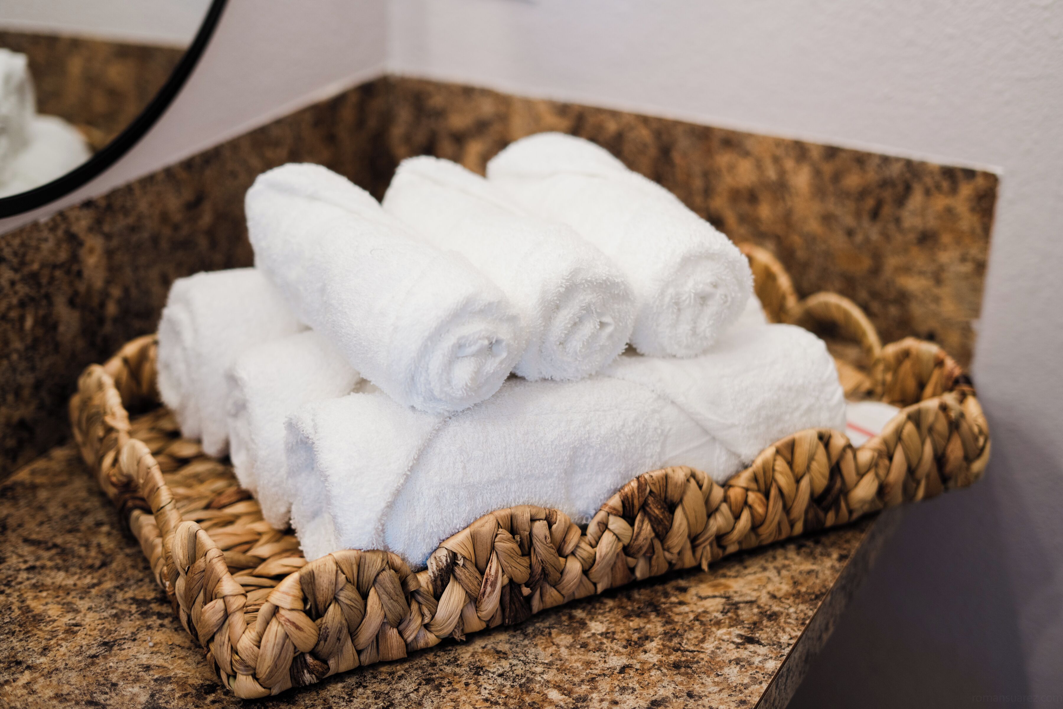 A woven basket containing neatly folded white towels on a granite countertop.