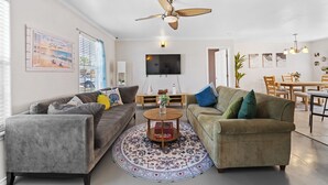 Ein Wohnzimmer mit zwei Sofas, einem Couchtisch, einem Deckenventilator und einem an der Wand montierten Fernseher.