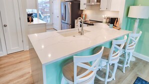 Una cocina moderna con una isla grande, armarios blancos e iluminación colgante.