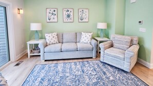 Una sala de estar con un sofá gris, un sillón a rayas y un tapete azul estampado. Hay dos lámparas de pared y tres obras de arte enmarcadas sobre el sofá.