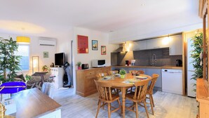 A modern kitchen with wooden cabinets, a built-in microwave, and a dishwasher. There is a dining area with a wooden table and chairs. - Maison des Bonheurs Océaniques - Welkeys (Capbreton)