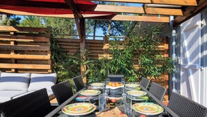 An outdoor dining area with a glass-top table, wicker chairs, and a wooden pergola overhead. - Maison des Bonheurs Océaniques - Welkeys (Capbreton)
