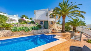 Una piscina con un muro in pietra e palme, circondata da un edificio bianco con un balcone.