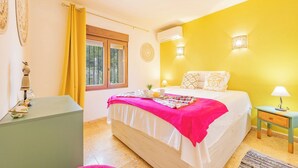 Un dormitorio con cama, mesitas de noche, una ventana y pared amarilla.
