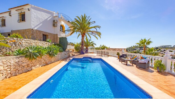 Una piscina con pared de piedra, una palmera y mobiliario de exterior.
