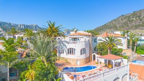 Una villa de estilo mediterráneo con piscina, rodeada de palmeras y con montañas al fondo.