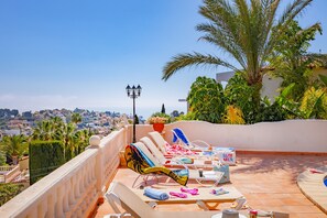 A rooftop terrace with sun loungers, a pool, and a view of a cityscape.