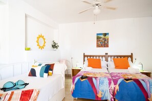 Une chambre avec deux lits, un ventilateur de plafond, un élément de décoration sur le thème du soleil, une petite plante et un tableau coloré accroché au mur.