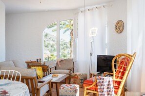A cozy living room with a TV, wicker furniture, and a view of palm trees.