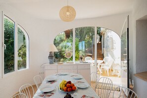 Un coin repas avec une table dressée pour quatre personnes, entourée de chaises blanches.
