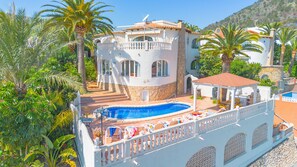 Una amplia villa con piscina, rodeada de exuberante vegetación y palmeras.