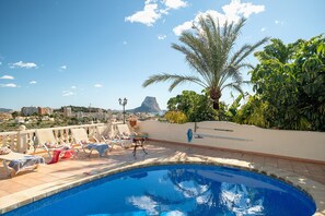 A rooftop pool area with lounge chairs and a view of the city and mountains.