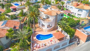 Un quartier résidentiel avec une grande maison dotée d’une piscine, de panneaux solaires et d’un balcon aménagé avec des chaises longues.