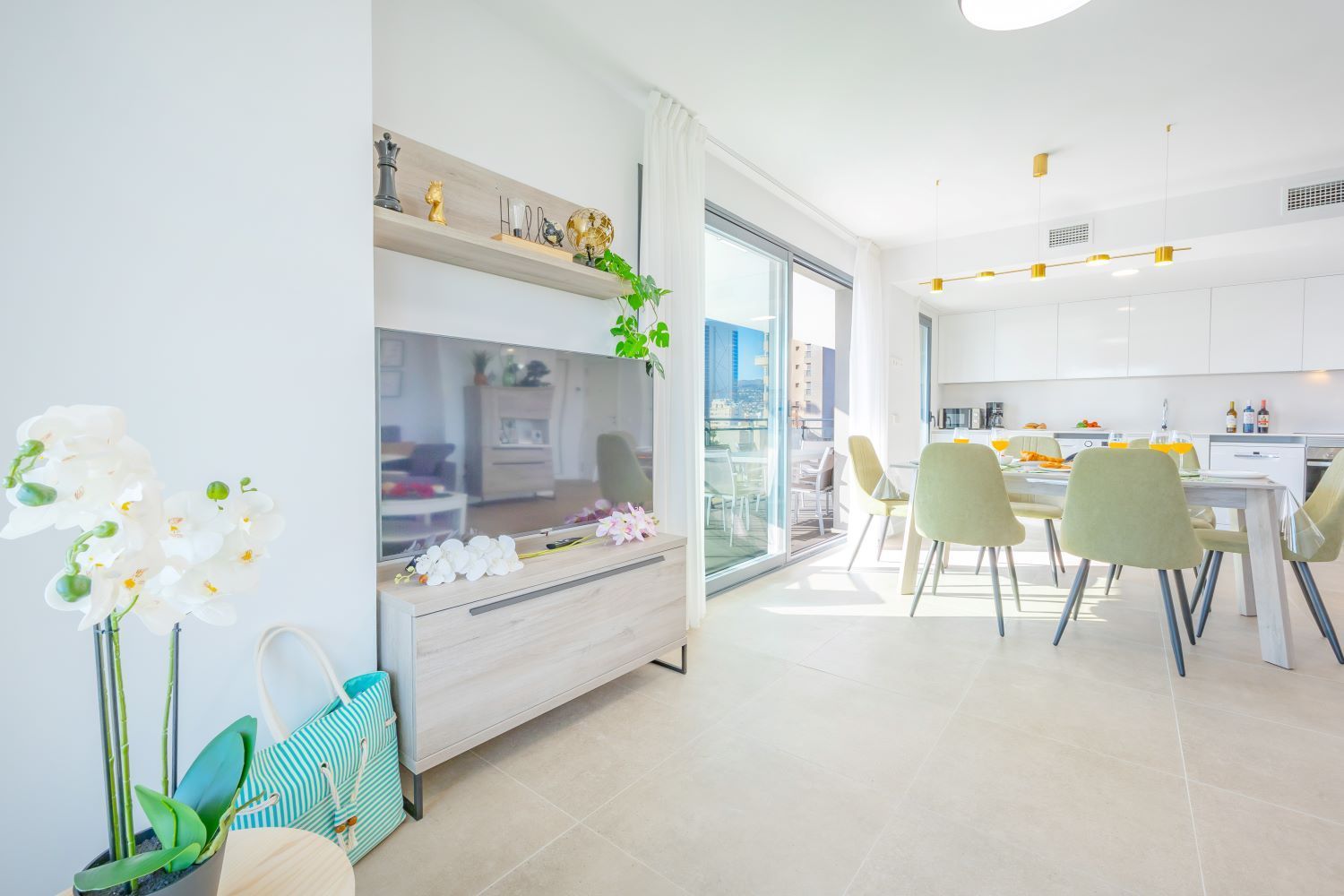 Una cocina moderna con armarios blancos, una zona de comedor con sillas y un ventanal grande.