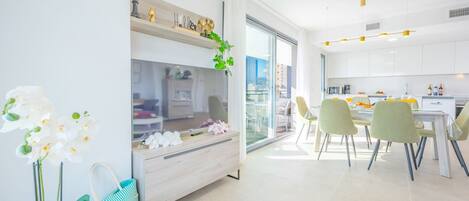 Una cocina moderna con armarios blancos, una zona de comedor con sillas y un ventanal grande.
