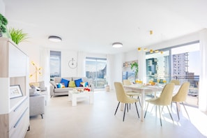 Een moderne woonkamer met een bank, salontafel, eethoek en grote ramen met uitzicht over de stad.