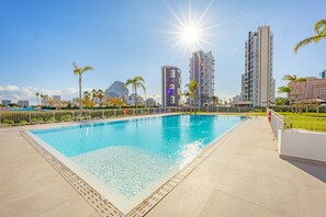 A swimming pool with a cityscape in the background, surrounded by palm trees and modern buildings.