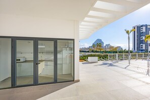 A modern building with a glass door entrance, a flat roof terrace, and a view of a cityscape with a prominent rock formation.