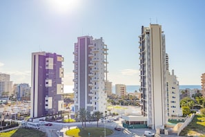 Een hoog appartementencomplex met meerdere balkons, een parkeerplaats en uitzicht op zee.