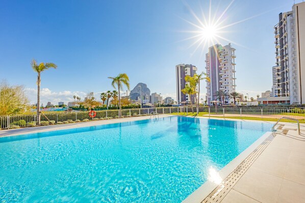 A swimming pool with a clear blue water surface, surrounded by a white fence, and tall buildings in the background.
