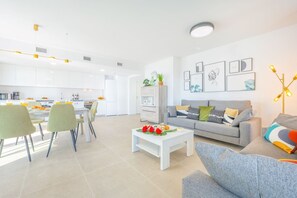 A modern living room with a grey sofa, a coffee table, and a dining area with chairs and a table.