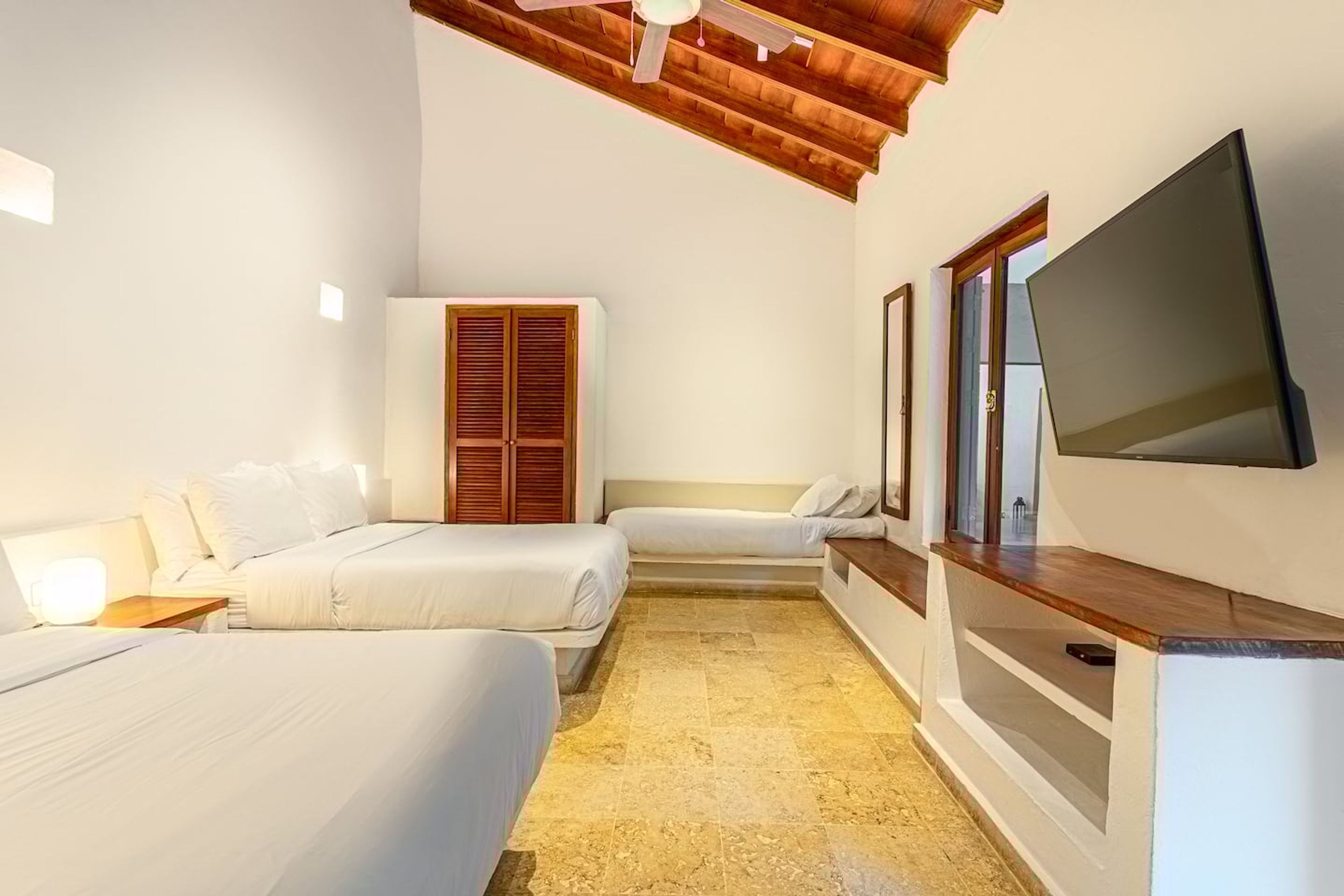 Une chambre d’hôtel avec deux lits, une télévision, des poutres apparentes en bois au plafond et un sol carrelé.