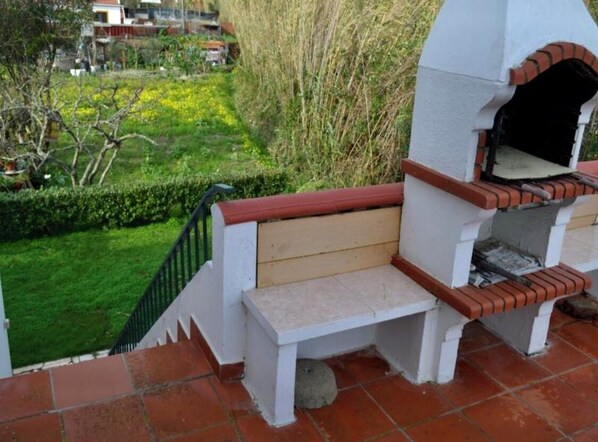 Un four en briques installé à l’extérieur, avec un banc et un escalier menant à un espace jardin.