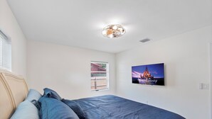 Ein Schlafzimmer mit einem Bett, einem Fenster mit Jalousien, einer Deckenleuchte und Wandkunst zum Thema Disney.
