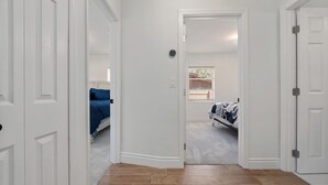Ein Flur, der in ein Schlafzimmer führt, mit einem Bett, einem Fenster mit Jalousien und einer Tür.