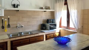 Een keuken met een dubbele spoelbak, houten kastjes, een magnetron en een blauwe kom op het aanrecht.