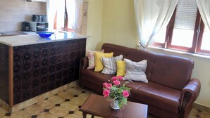 Een woonkamer met een bruine leren bank, een salontafel met een bloevas, en een keukenhoek met een magnetron en een koffiezetapparaat.