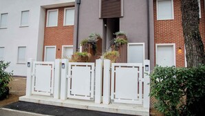 Un edificio moderno con fachada de ladrillo, contraventanas blancas y entrada protegida con plantas en macetas.