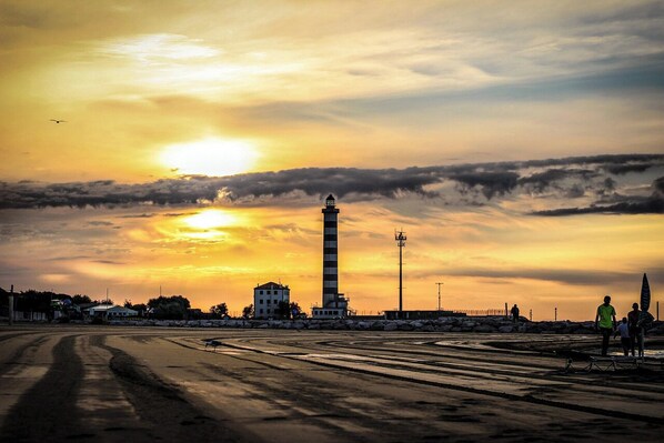 Un phare au coucher du soleil, avec un ciel dégagé, une plage de sable et quelques personnes à proximité.